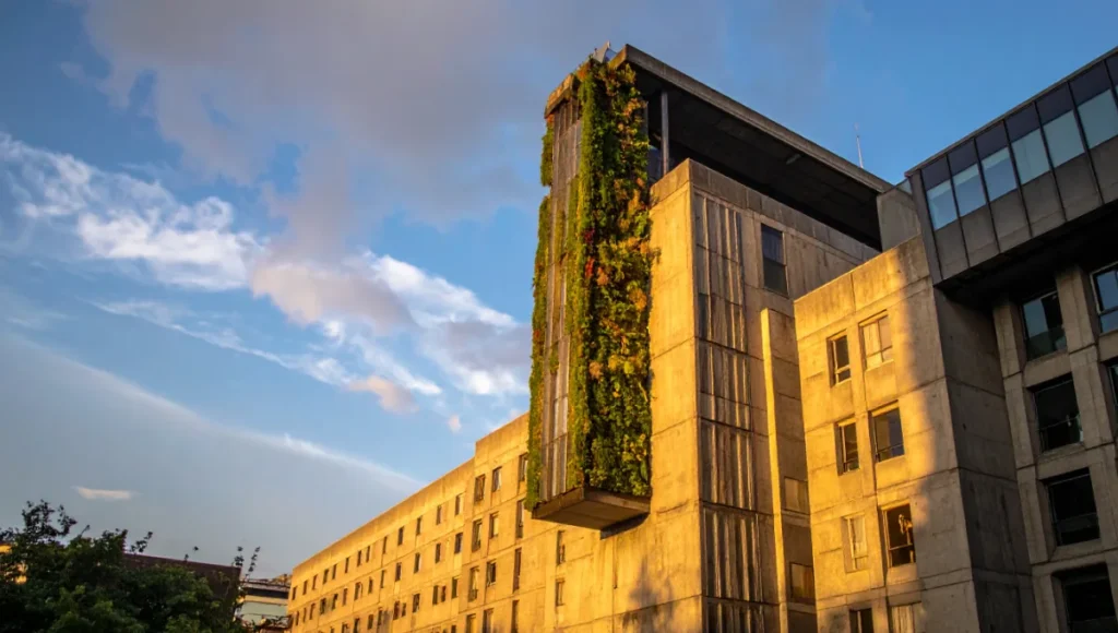 Ultra-realistic photograph of Nuvira Space's "The Monolith Reborn" retrofitted brutalist high-rise in London, showcasing carbon-negative upgrades including BIPV solar shading fins, algae bio-curtains for CO2 scrubbing, graphite-infused concrete coating, and preserved raw béton brut facade during golden hour architectural photography.