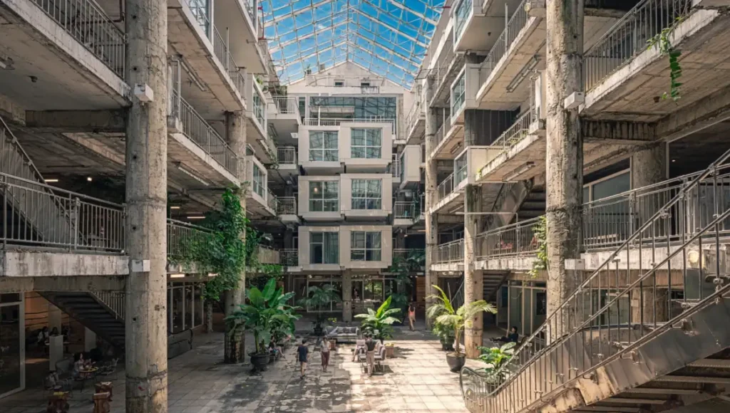 Ultra-realistic architectural rendering of Nuvira Space's Neural Hive 01 mall adaptive reuse housing project in a tropical Da Nang-style environment, showcasing kinetic residential voxel pods within a steel skeleton atrium with vertical tropical forests, brushed brass facades, raw concrete textures, AI utility spines, and hyper-mixed-use commons for sustainable high-density urban living and carbon reduction.