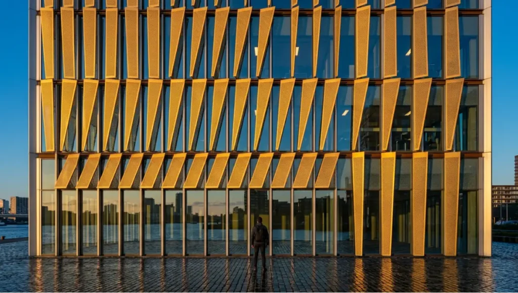 Kinetic aluminium louvre facade on a high-rise commercial tower in Rotterdam at golden hour, 3,840 independently addressable perforated panels angled at 25 degrees casting geometric shadow patterns across fritted inner glazing, 24mm tilt-shift architectural photography, anodised silver and deep navy colour palette, kinetic facade energy performance system in operation.